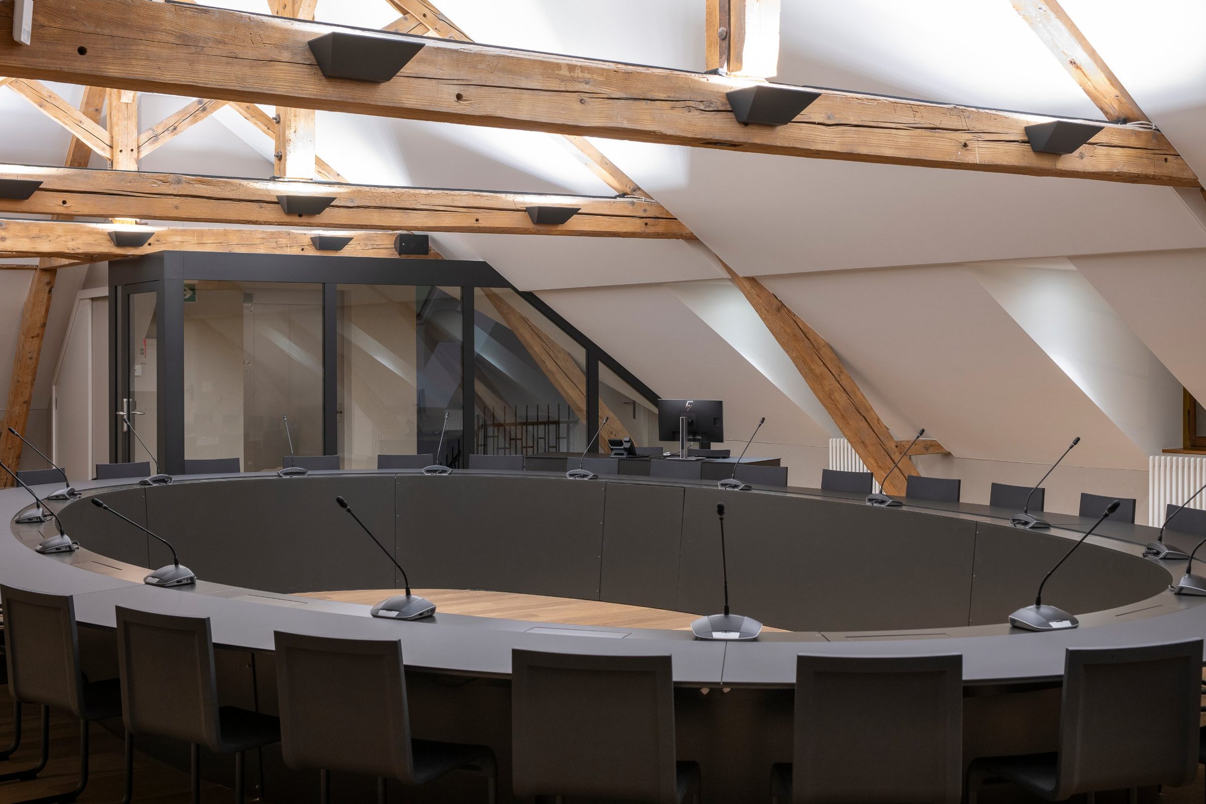 Salle du Conseil communal de Chêne-Bourg sous la charpente en bois, grande table ovale sombre